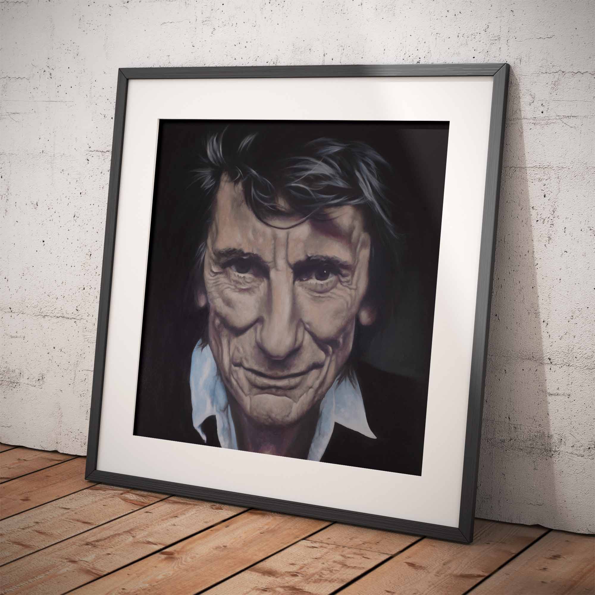 Framed portrait of Ronnie Wood on a wooden floor with a white brick wall background