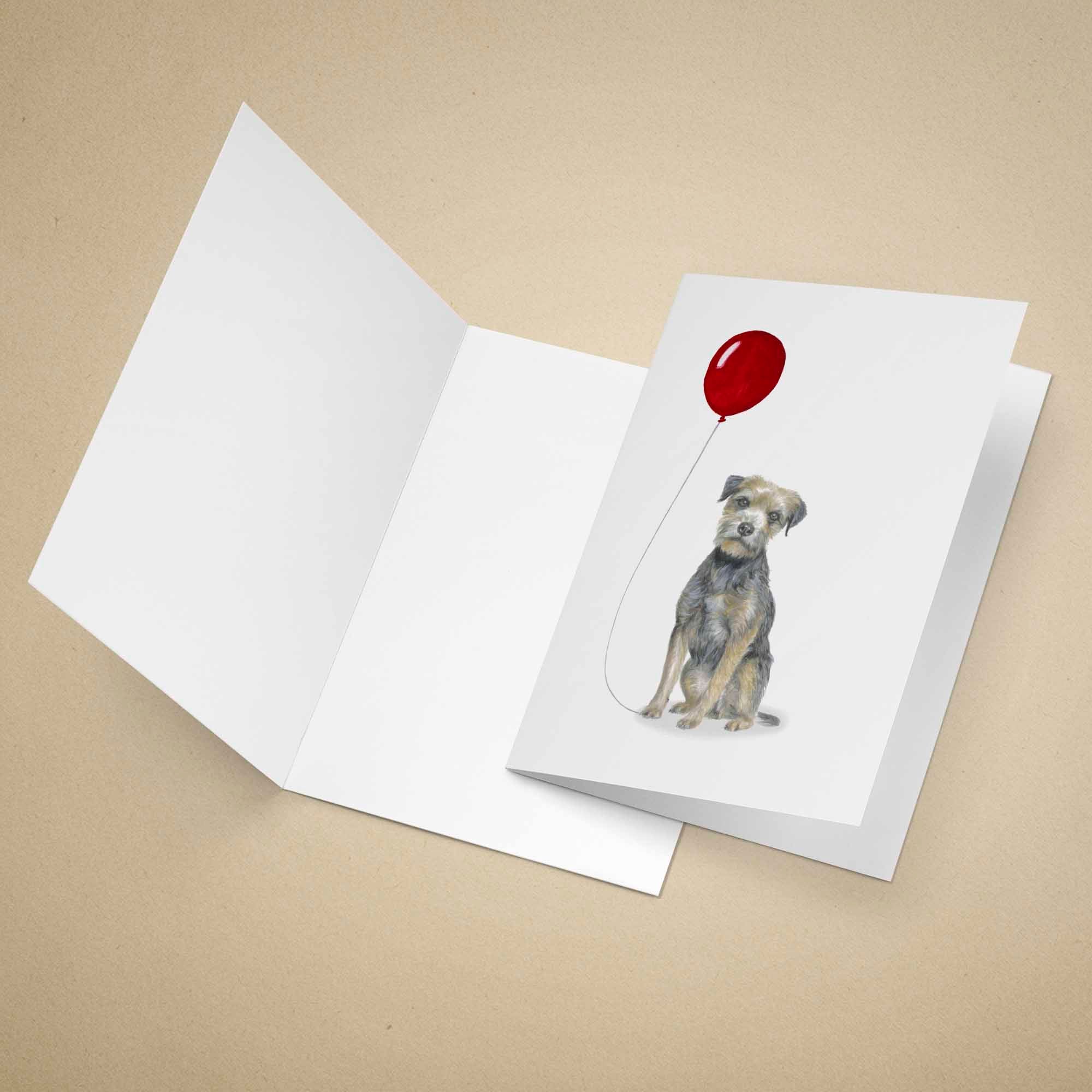 Greeting card with a Border Terrier holding a red balloon on a beige background