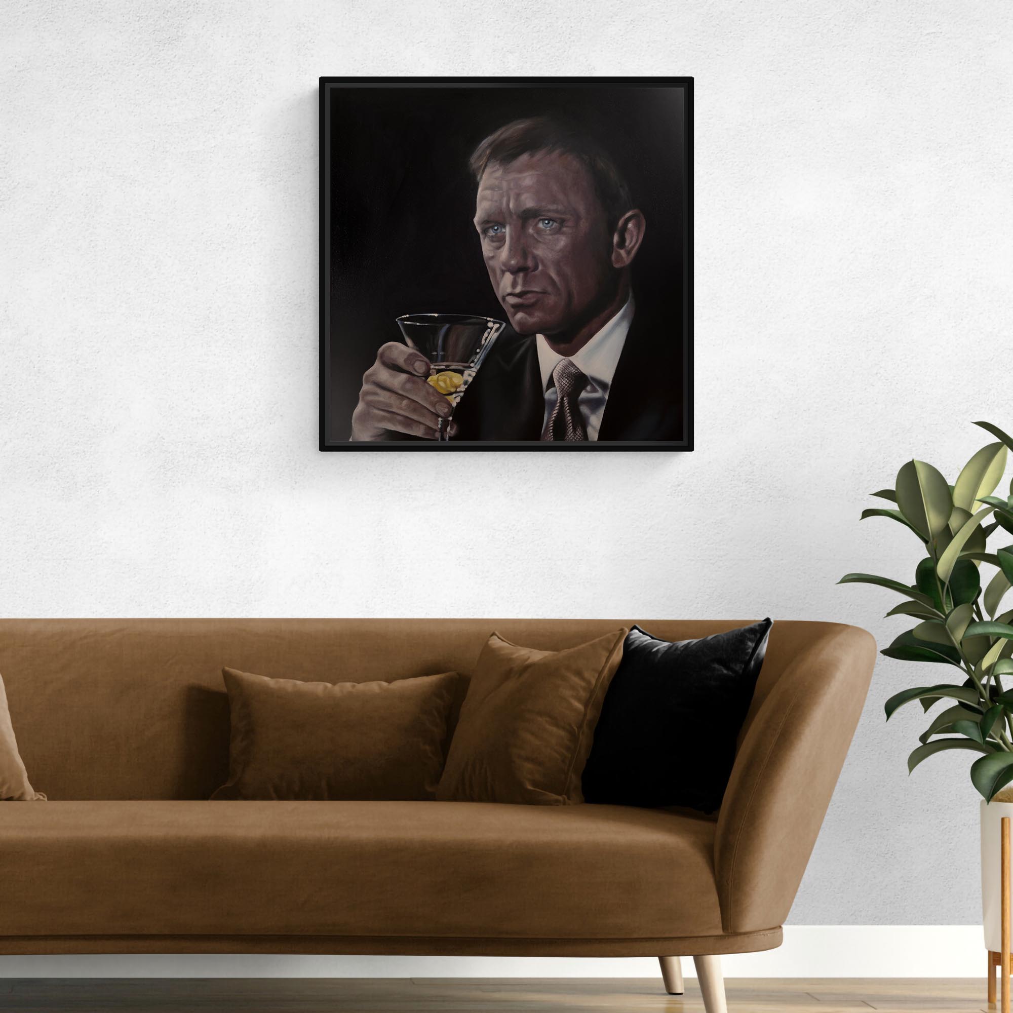Framed portrait of James Bond, Daniel Craig holding a glass above a brown sofa with decorative pillows.