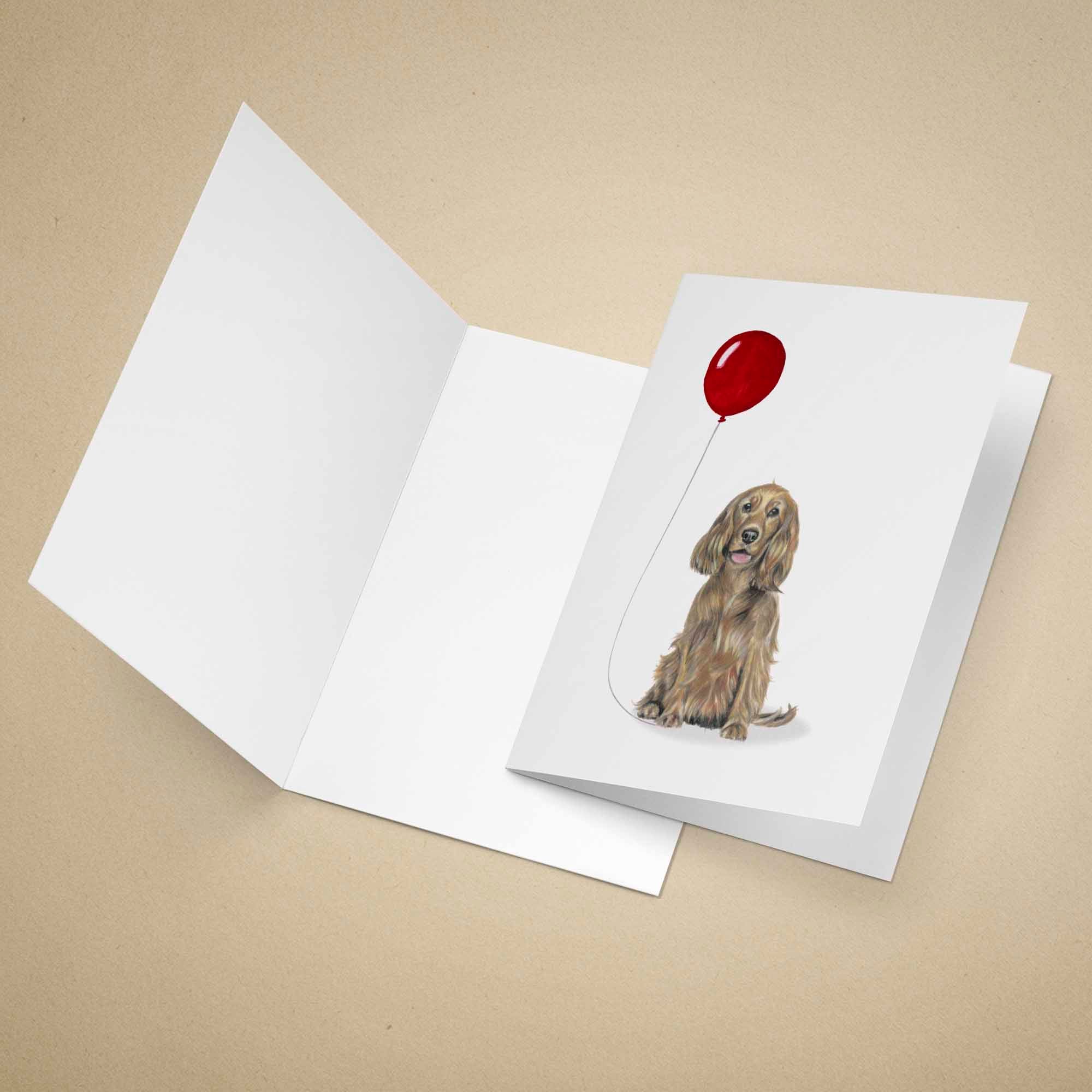 Greeting card with a golden brown Cocker Spaniel holding a red balloon on a beige background