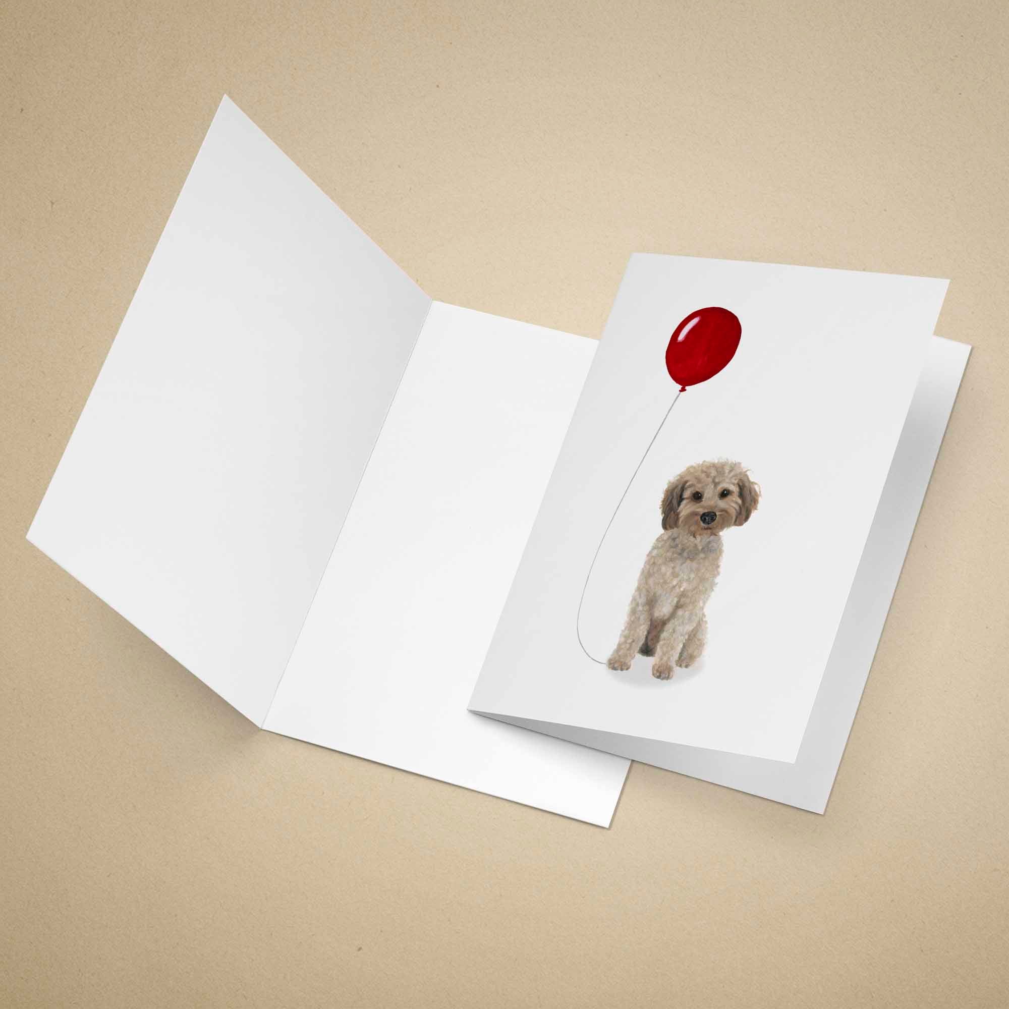 Greeting card with a light brown Cockapoo holding a red balloon on a beige background