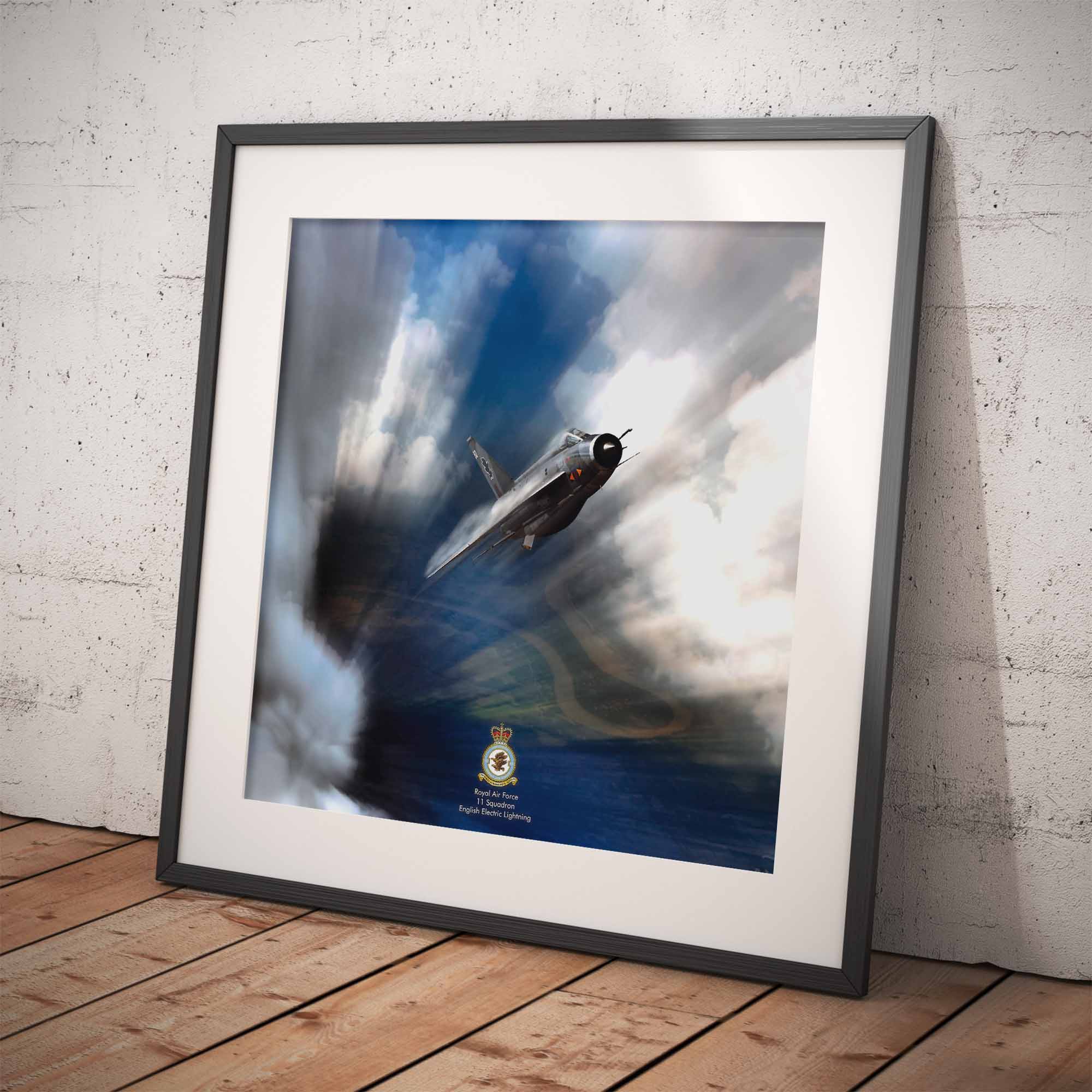 Framed artwork of an English Electric Lightning airplane in flight with a logo at the bottom, on a wooden floor against a white brick wall.