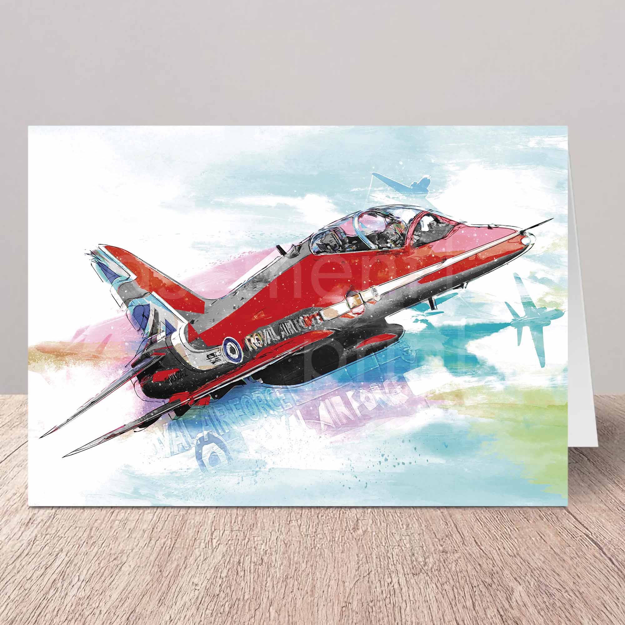 Greeting card of a Red Arrows aircraft on a white wall with wooden table top