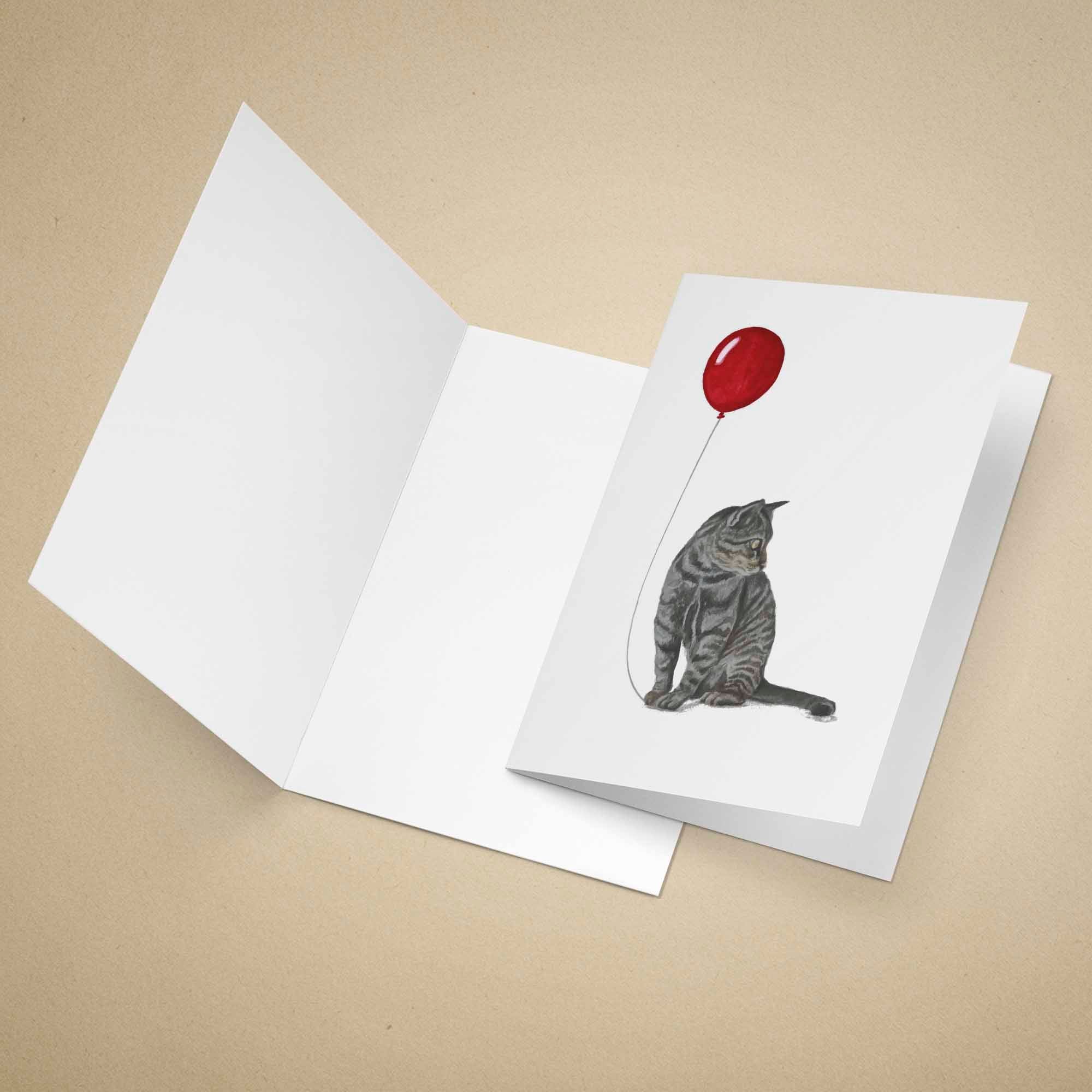 Greeting card with a grey tabby cat and red balloon design on a beige background