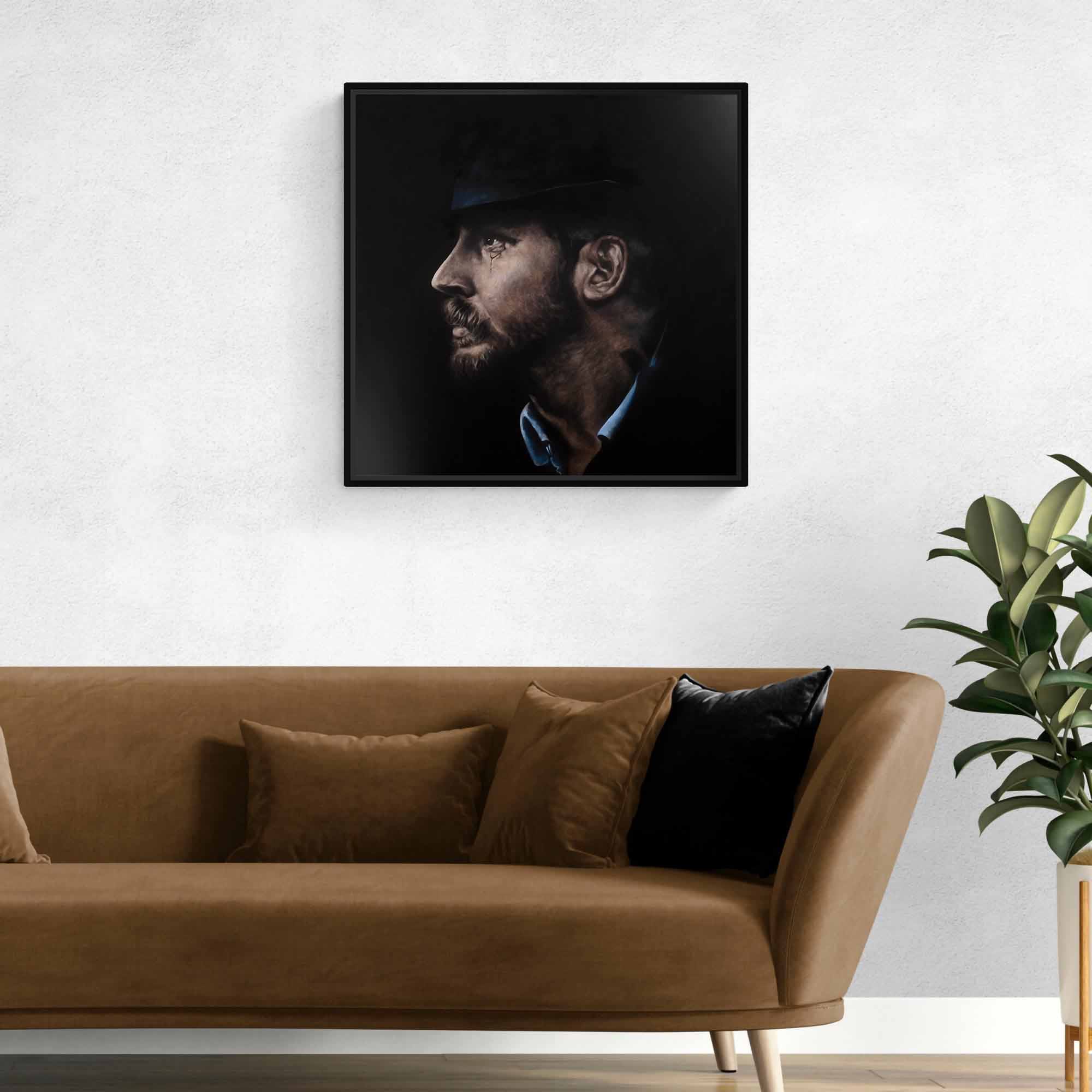 Framed portrait of Tom Hardy above a brown sofa with decorative pillows in a living room setting.