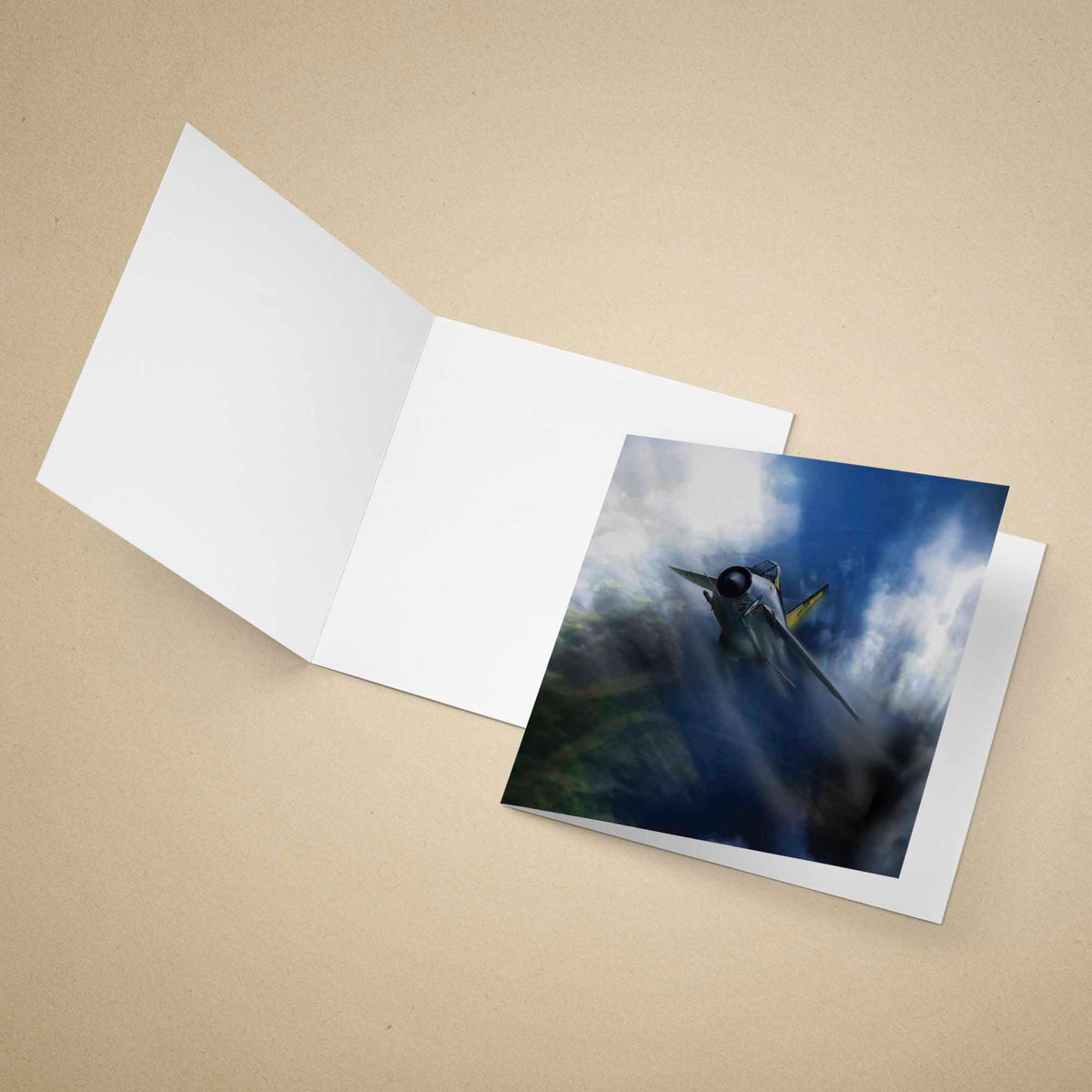 An open white greeting card on a beige background, with a printed photo of a fighter jet flying through clouds.
