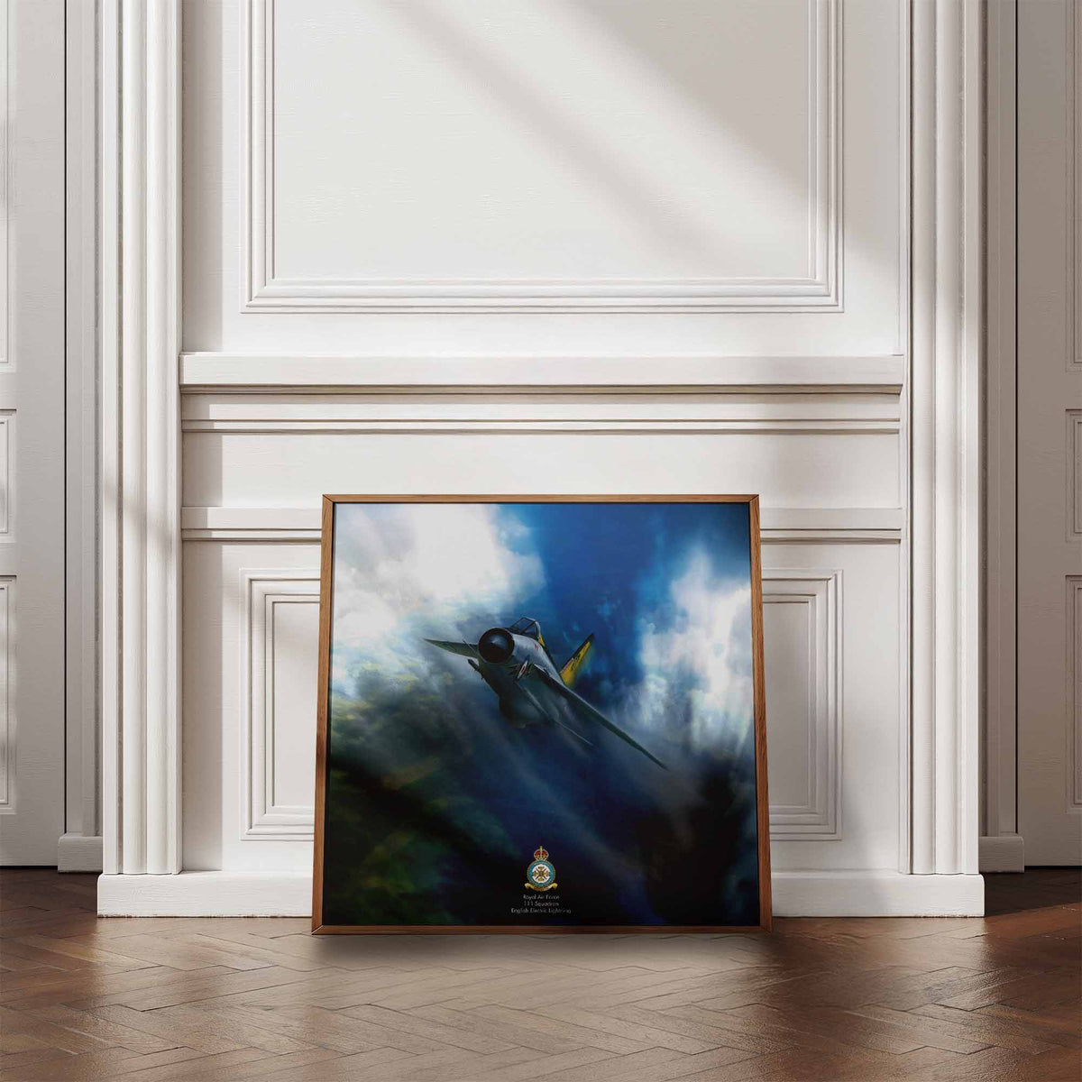 A framed art print depicting a fighter jet flying through dramatic blue and white clouds, leaning against a white paneled wall on a wooden floor.