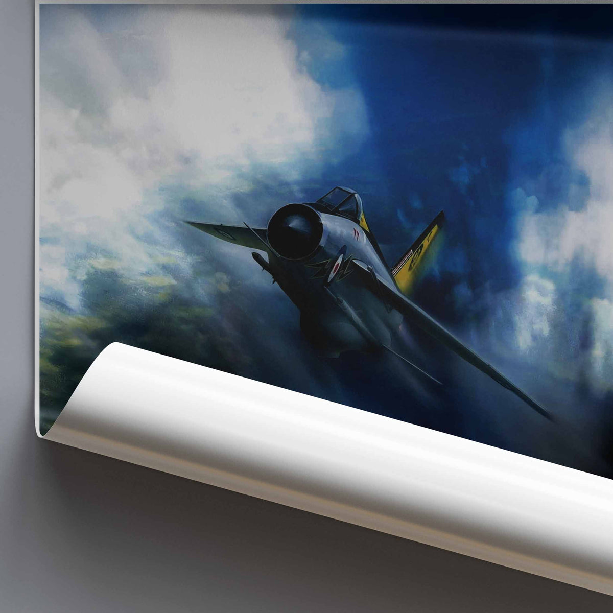 A rolled poster or wall art print showing a vintage fighter jet flying through dramatic blue and white clouds, photographed against a dark gray background.