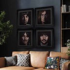 Framed portraits of each member of The Beatles on a wall above a couch with decorative pillows.