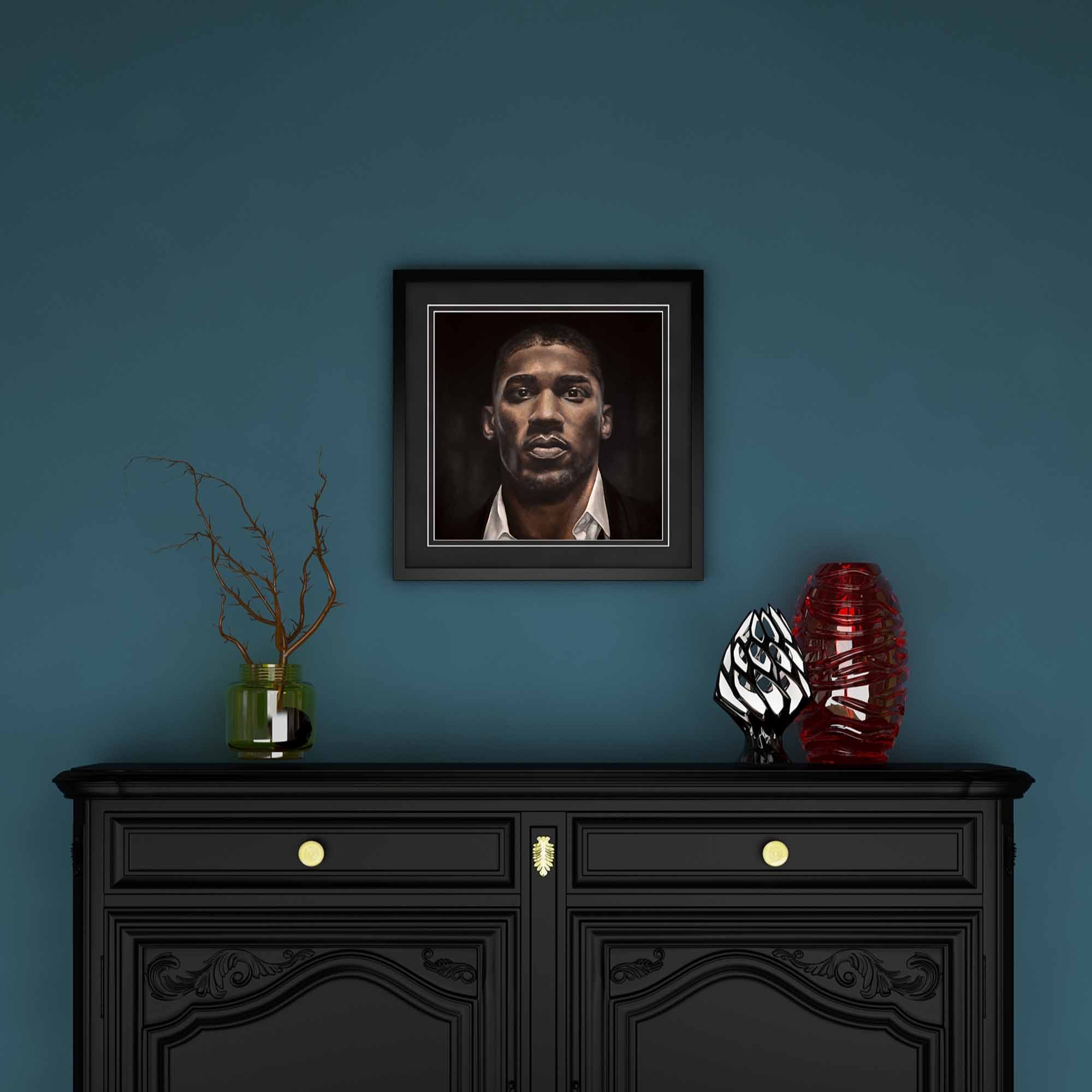 Framed oil painting of the boxer Anthony Joshua on a blue background above a black cabinet.