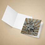 An open white greeting card on a beige background, with the front insert showing a printed illustration of an Apache AH-64 military helicopter over a brown and gray sunburst design with the text 'APACHE AH-64'.