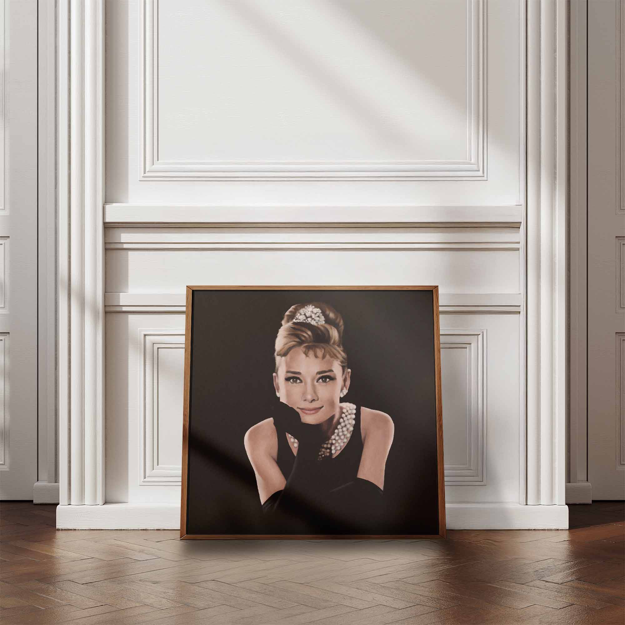 Framed portrait of Audrey Hepburn in a black dress with a tiara on a white wall.