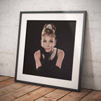 Framed portrait of Audrey Hepburn with a stylish updo and pearl necklace on a wooden floor.