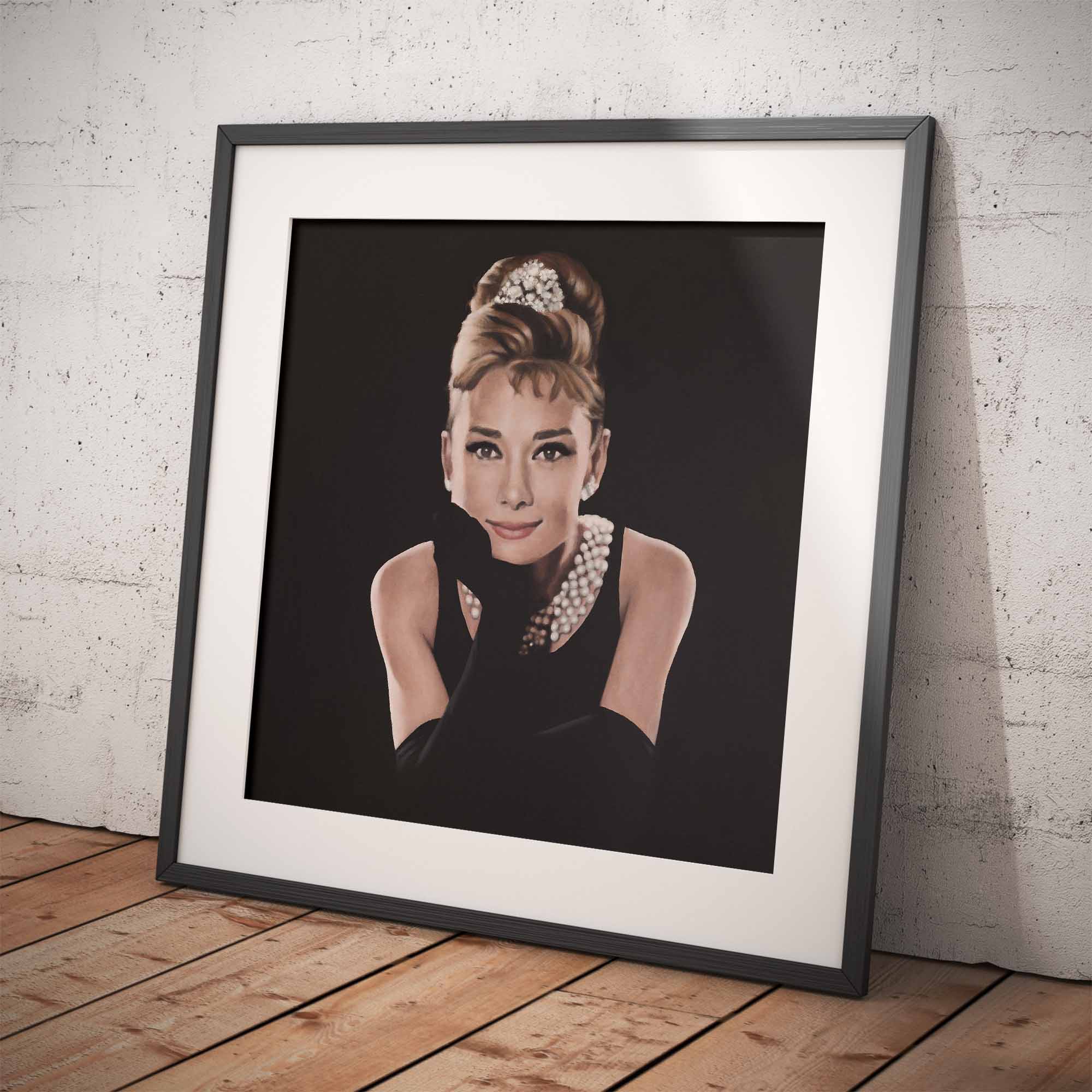 Framed portrait of Audrey Hepburn with a stylish updo and pearl necklace on a wooden floor.
