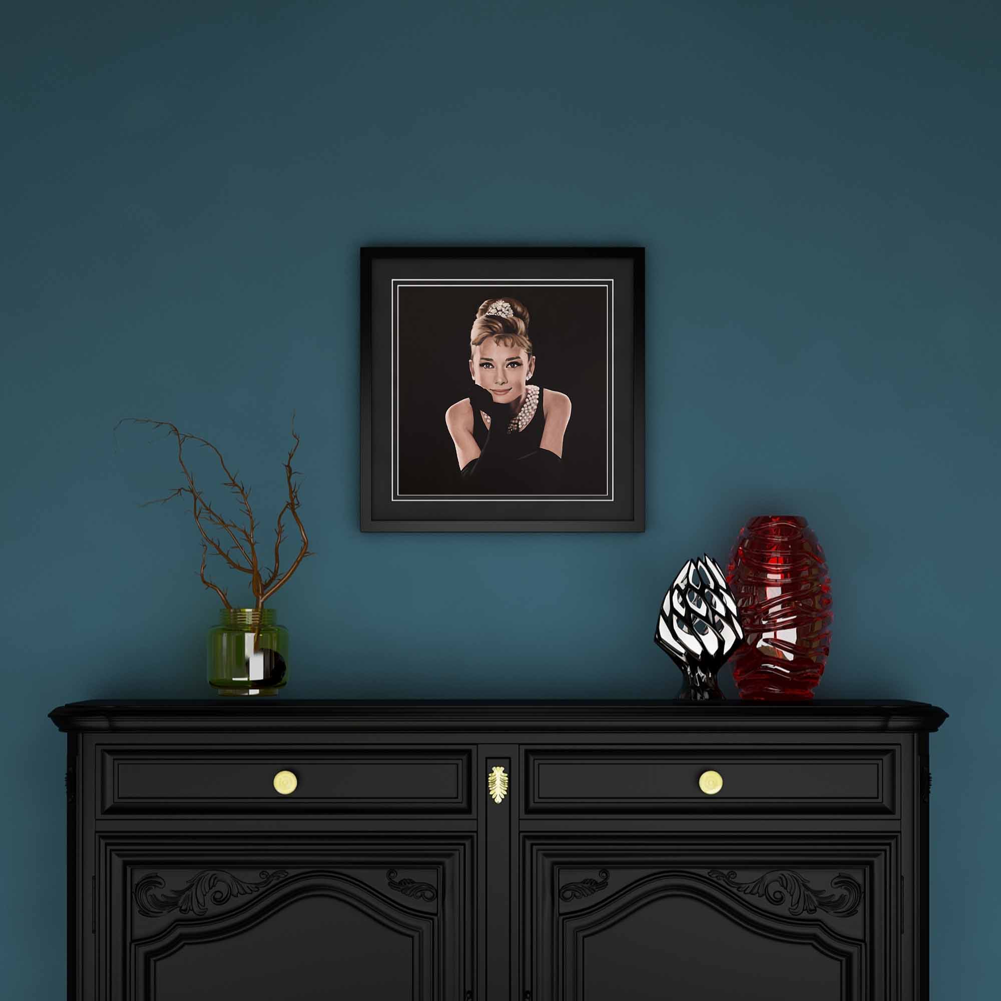 Framed portrait of Audrey Hepburn above a black cabinet with decorative items against a blue wall