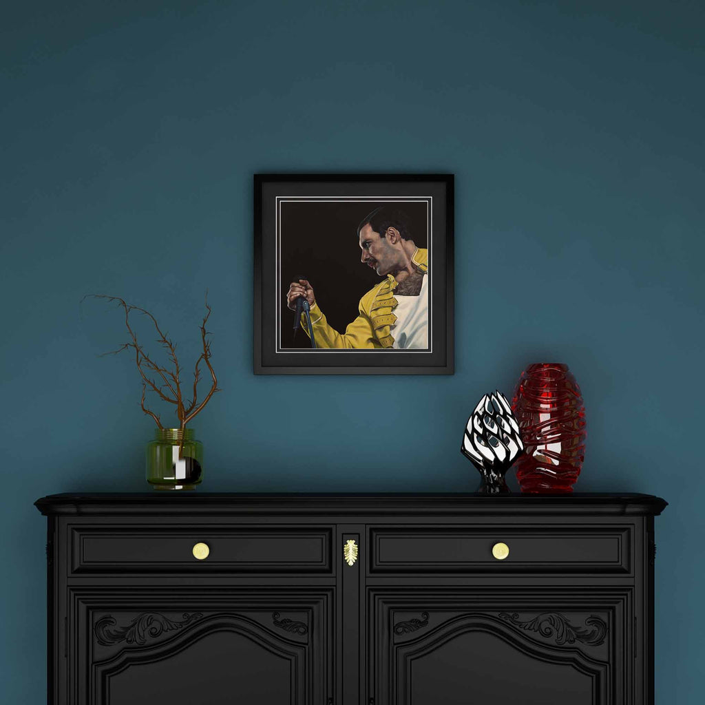 Framed artwork of Freddie Mercury on a blue wall above a black cabinet with decorative items.