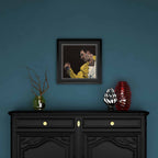 Framed artwork of Freddie Mercury on a blue wall above a black cabinet with decorative items.