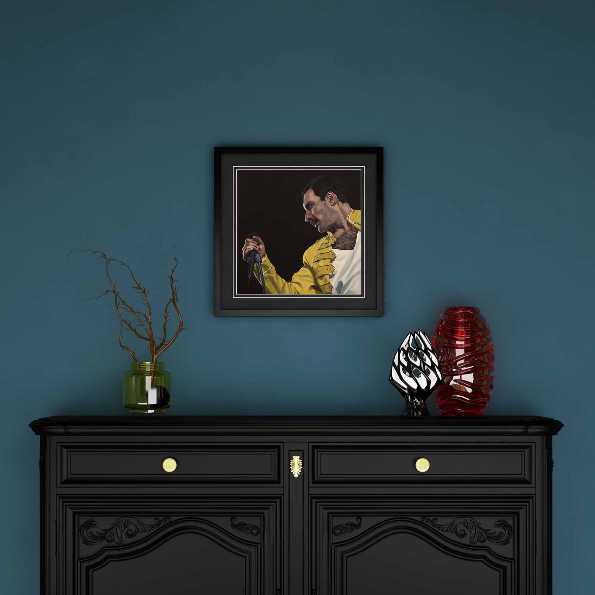 Framed artwork of Freddie Mercury on a blue wall above a black cabinet with decorative items.