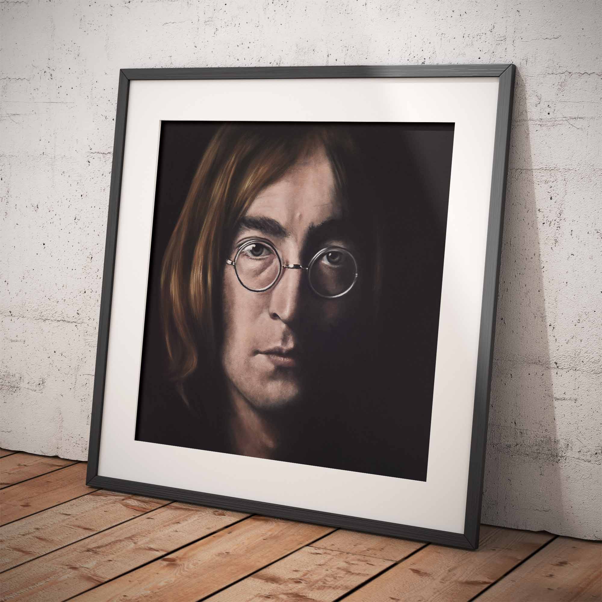 Framed portrait of John Lennon on a wooden floor against a white brick wall.