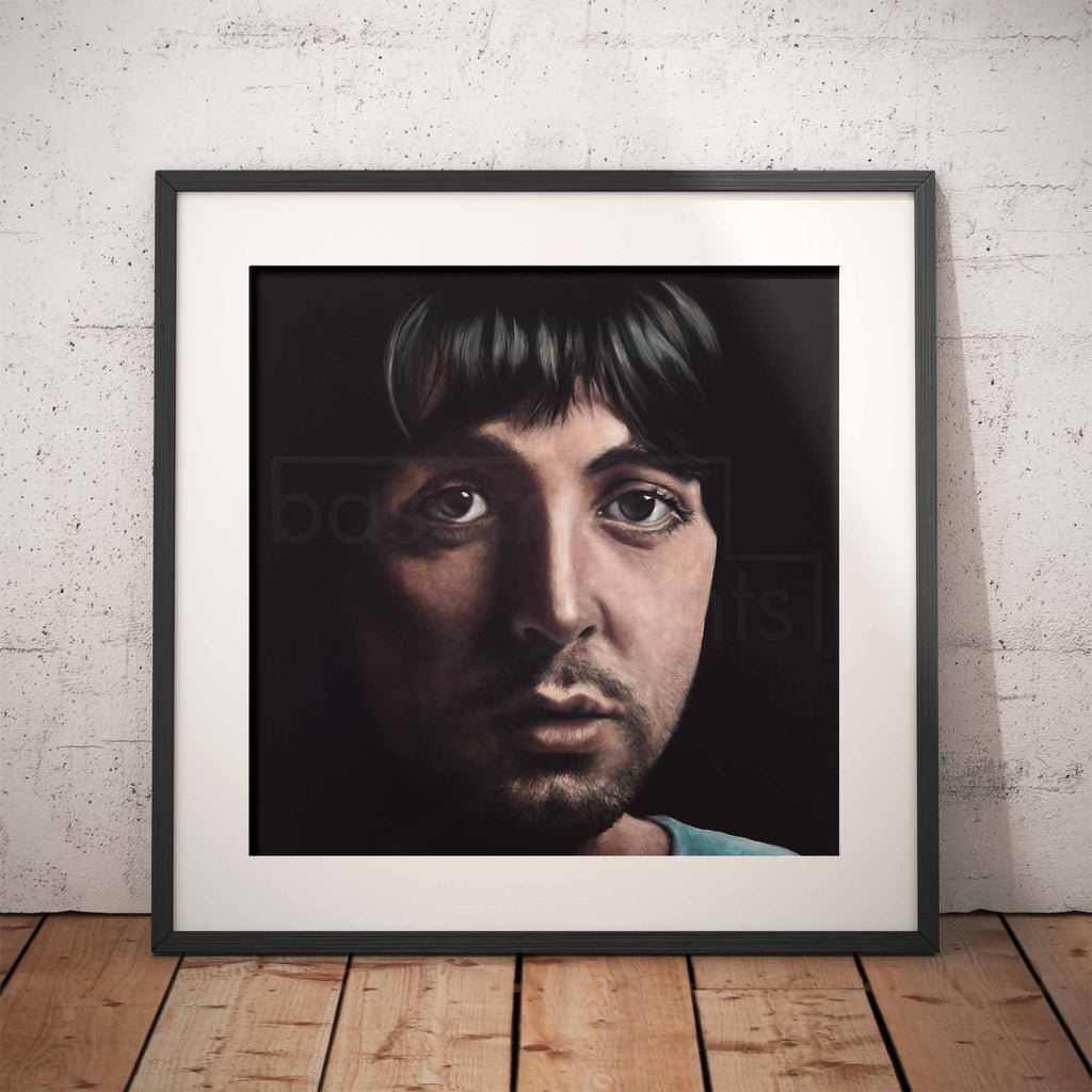 Framed portrait of Paul McCartney against a white brick wall.