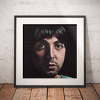 Framed portrait of Paul McCartney against a white brick wall.