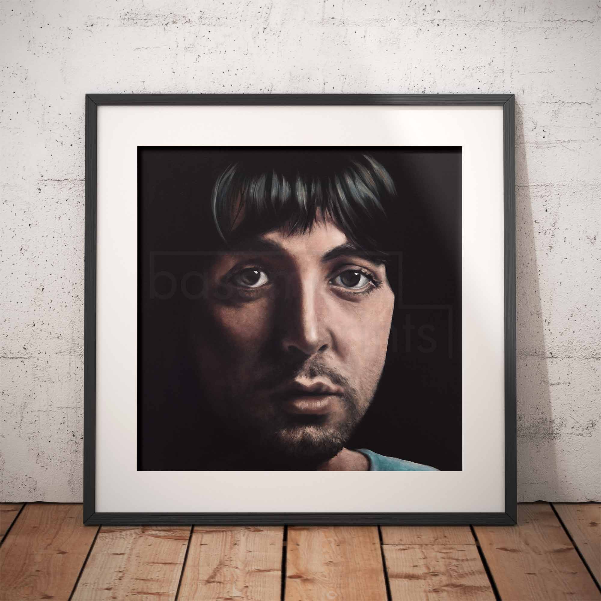 Framed portrait of Paul McCartney against a white brick wall.