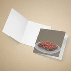 An open white greeting card lies on a beige background, with a printed card insert showing an oil painting of baked beans on toast.