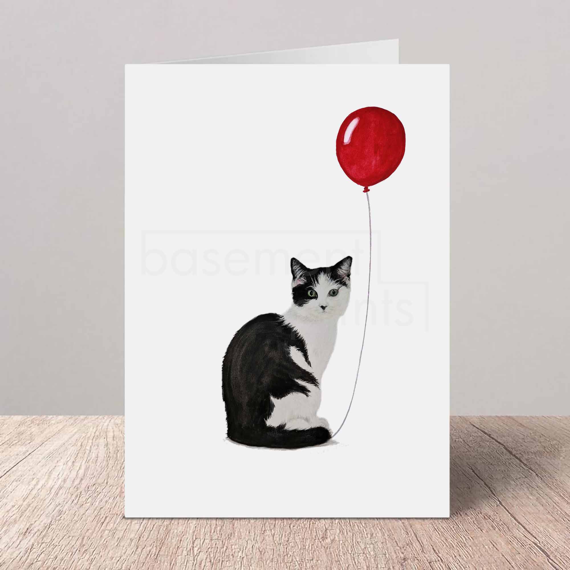 Greeting card with a black and white cat holding a red balloon on a white background
