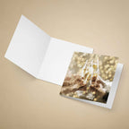 An open white greeting card lies on a beige background, with a printed insert or photo card showing an abstract champagne-themed design partially tucked inside.