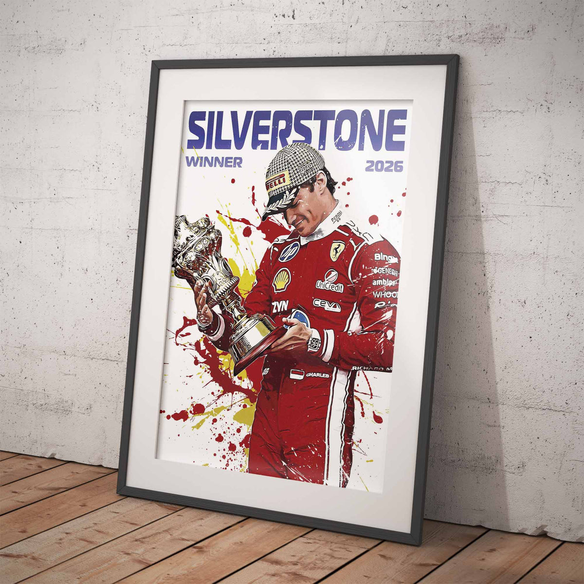 A framed art print leaning against a textured gray wall on a wooden floor. The print features a stylized illustration of Formula 1 driver Charles Leclerc wearing his red Ferrari racing suit and holding the Silverstone trophy, with the text 'SILVERSTONE WINNER 2026'.