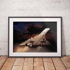 A framed art print of a Concorde supersonic jet against a dramatic sunset sky, leaning against a white brick wall on a wooden floor.