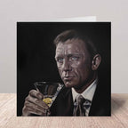 Greeting card Daniel Craig as James Bond holding a cocktail glass on a wooden surface.