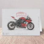 Agreeting card featuring a stylized Ducati motorcycle illustration on a white grid background, displayed standing on a light wood surface against a pale wall.