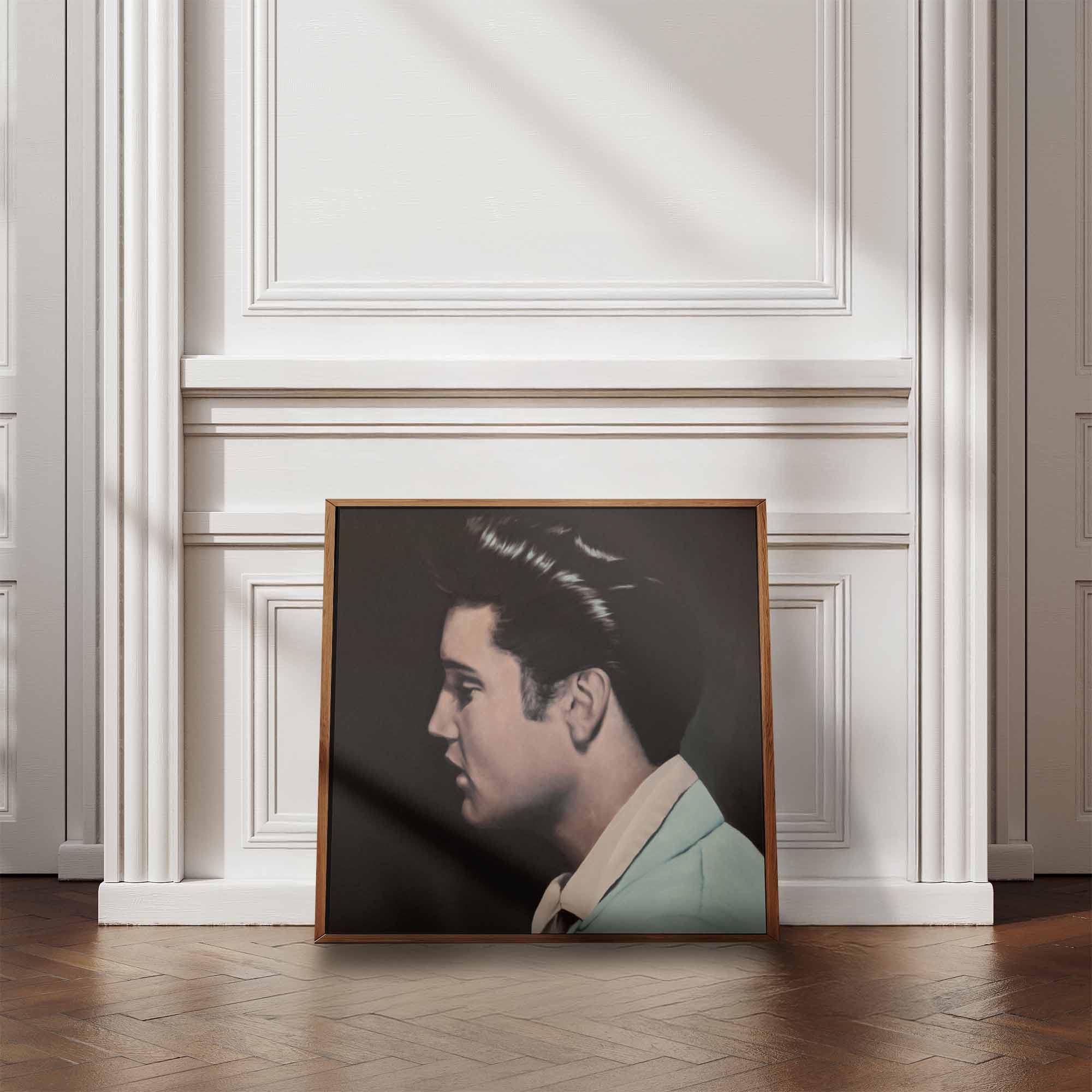Framed portrait of Elvis Presley in a formal attire on a wall with decorative molding.