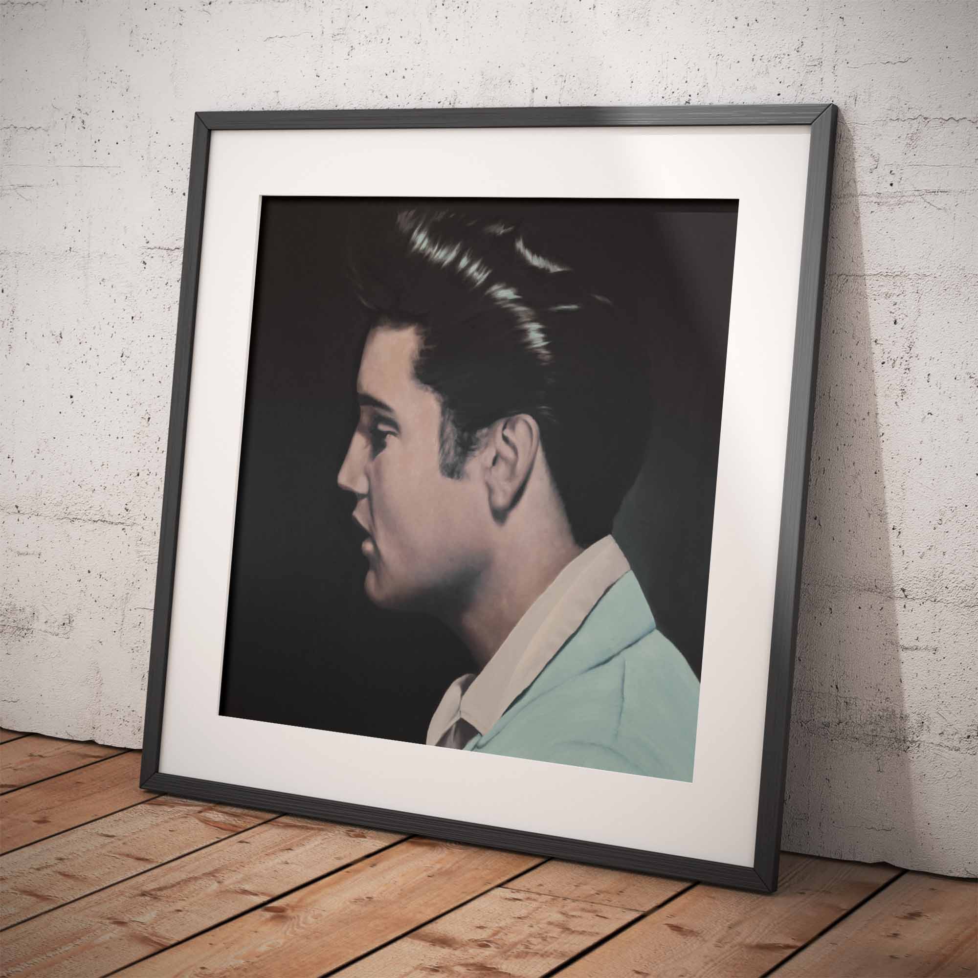 Framed portrait of Elvis Presley against a white brick wall.