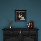 Framed portrait of Elvis Presley above a black cabinet with decorative items on a blue wall