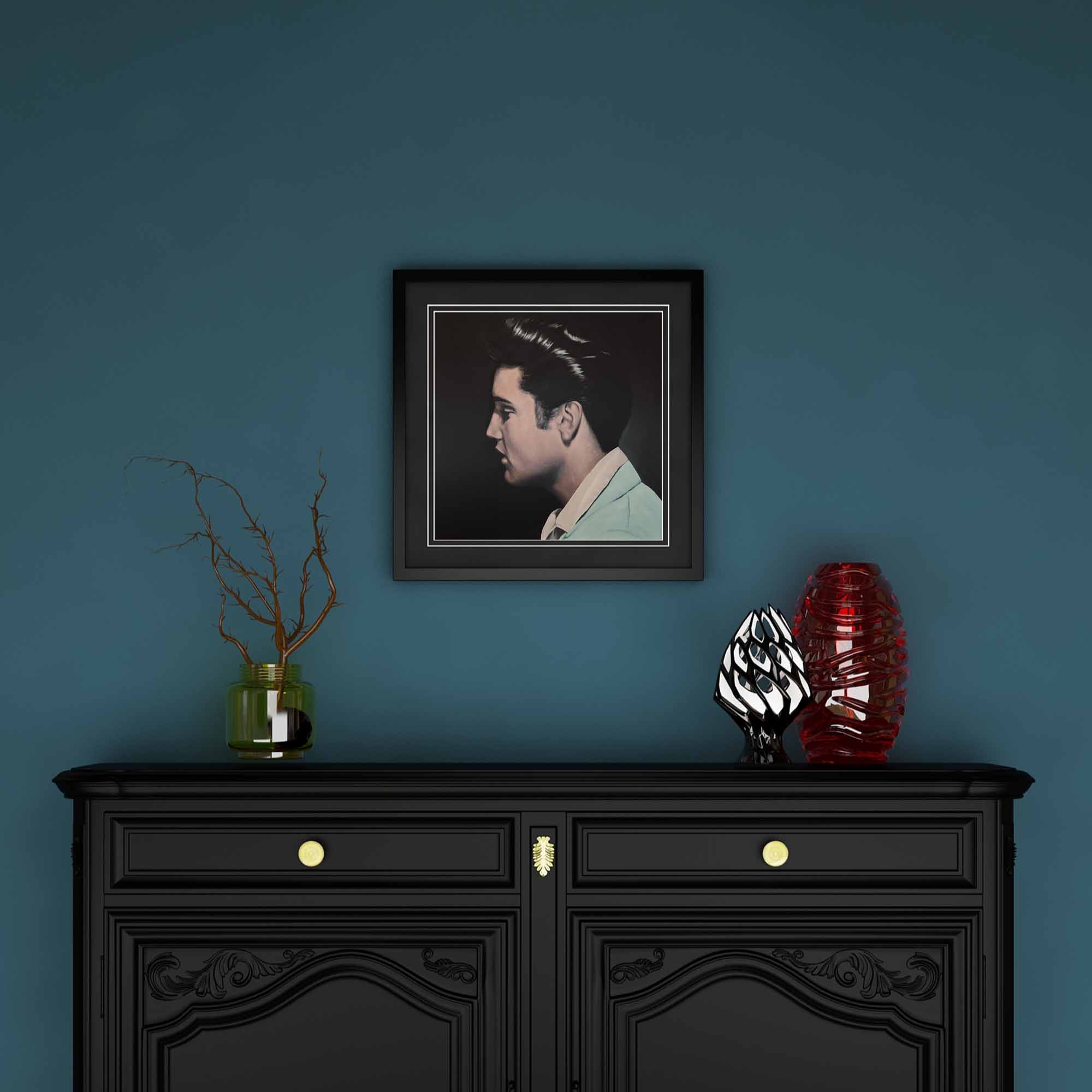 Framed portrait of Elvis Presley above a black cabinet with decorative items on a blue wall