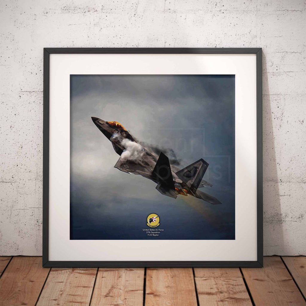 Framed photograph of an F22 Raptor fighter jet in flight against a cloudy sky on a wooden floor with white brick wall background.