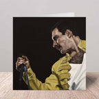 Greeting card with a portrait of Freddie Mercury in a yellow jacket holding a microphone on a wooden surface.