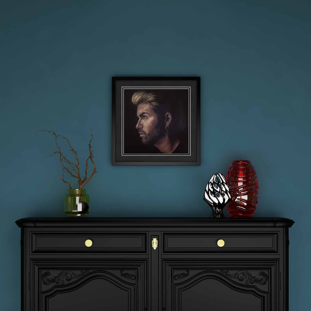 Framed portrait of George Michael above a black cabinet with decorative items against a blue wall