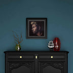 Framed portrait of George Michael above a black cabinet with decorative items against a blue wall
