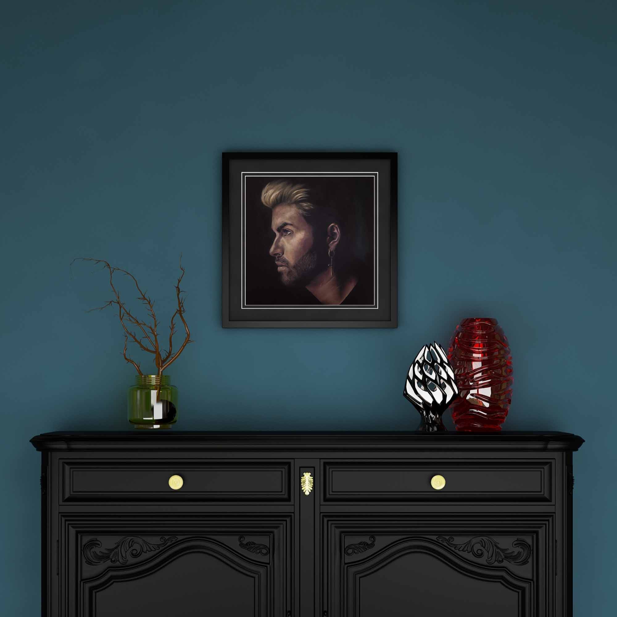 Framed portrait of George Michael above a black cabinet with decorative items against a blue wall