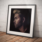 Framed portrait of George Michael on a wooden floor against a white brick wall.