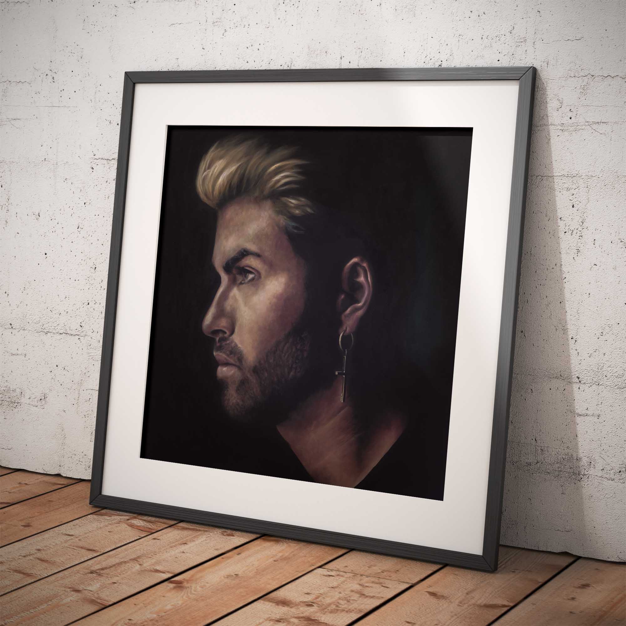 Framed portrait of George Michael on a wooden floor against a white brick wall.