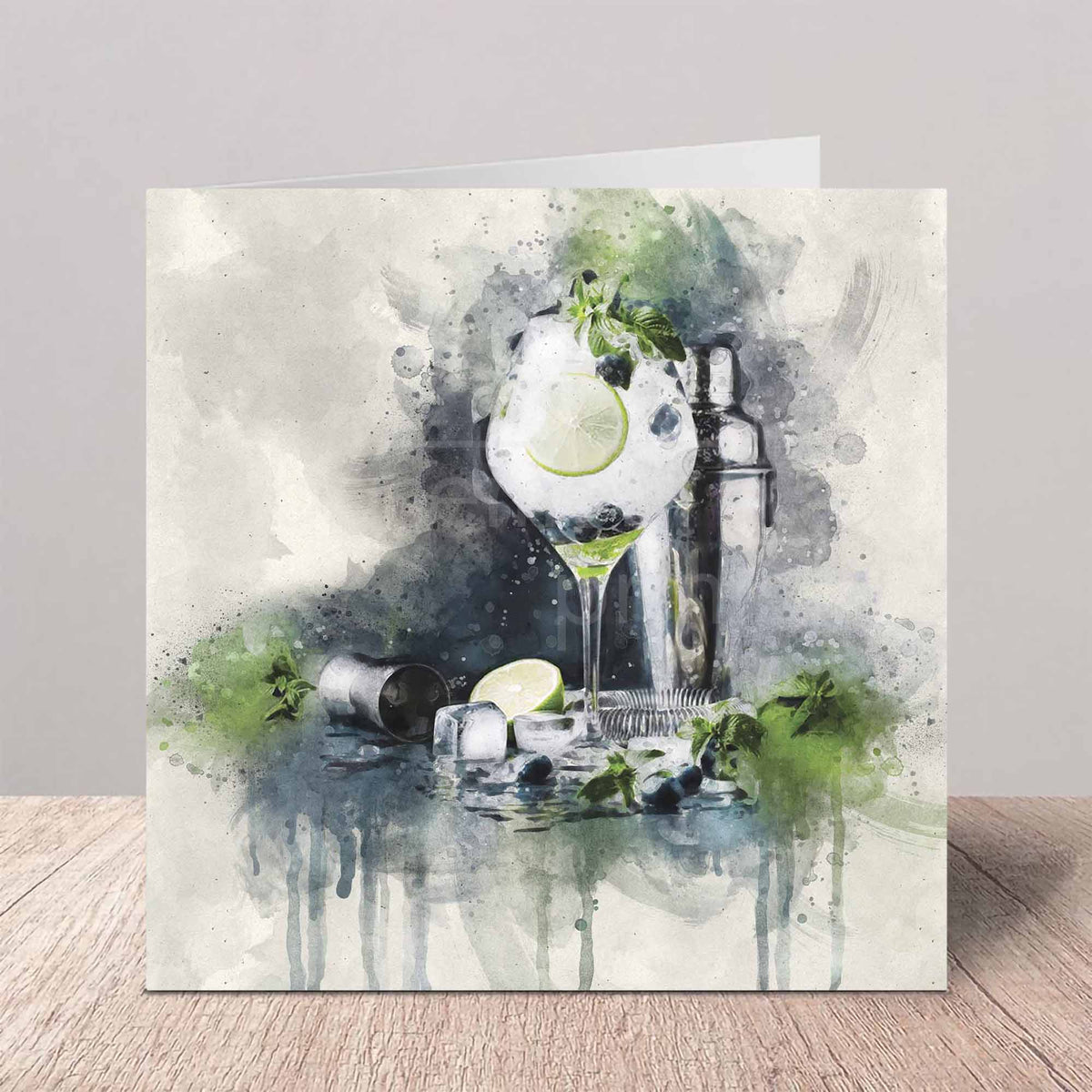 A square greeting card featuring a watercolor illustration of a gin and tonic with a lime slice, ice, mint leaves, and a shaker, standing on a wooden surface against a neutral gray background.
