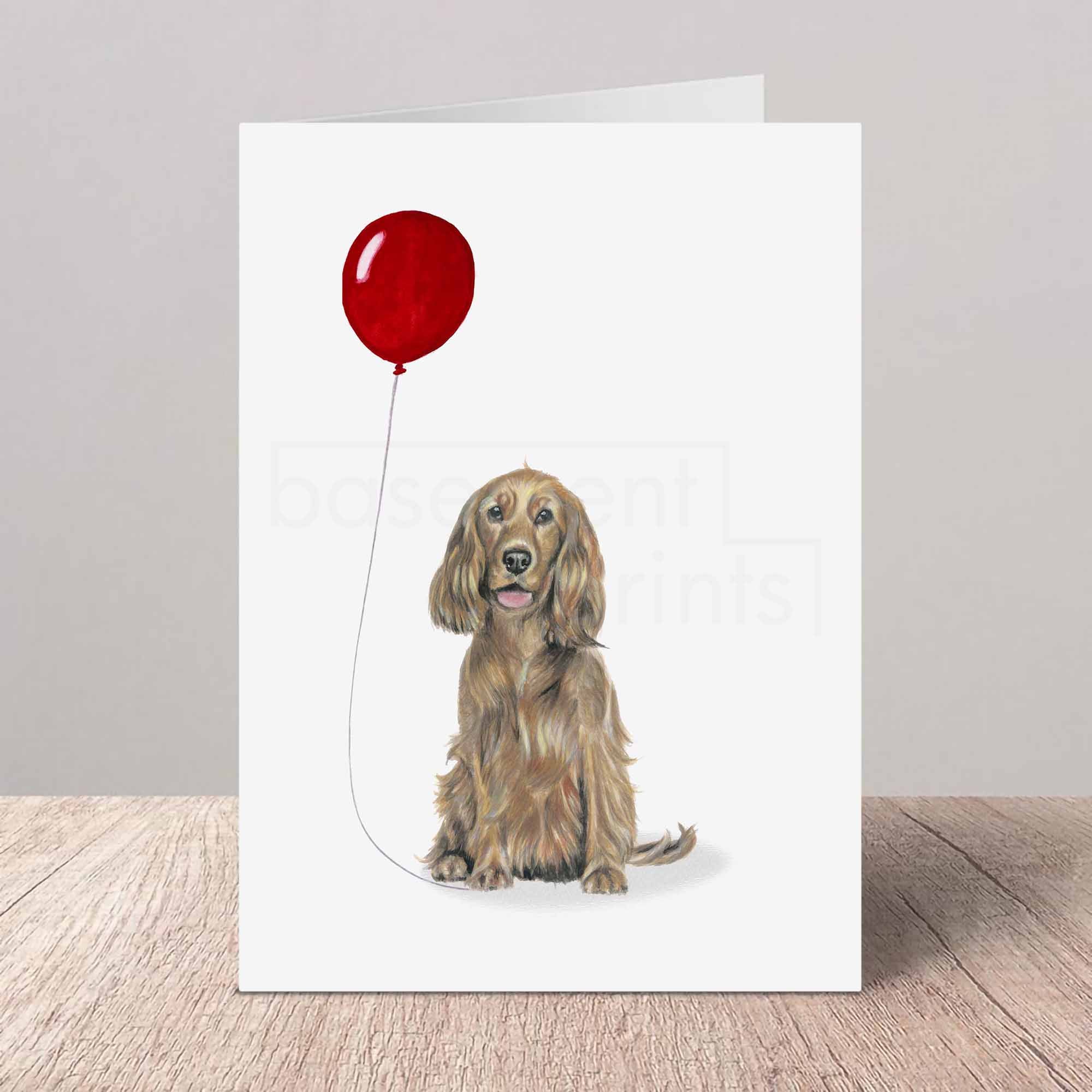 Greeting card with a golden brown Cocker Spaniel holding a red balloon on a white background