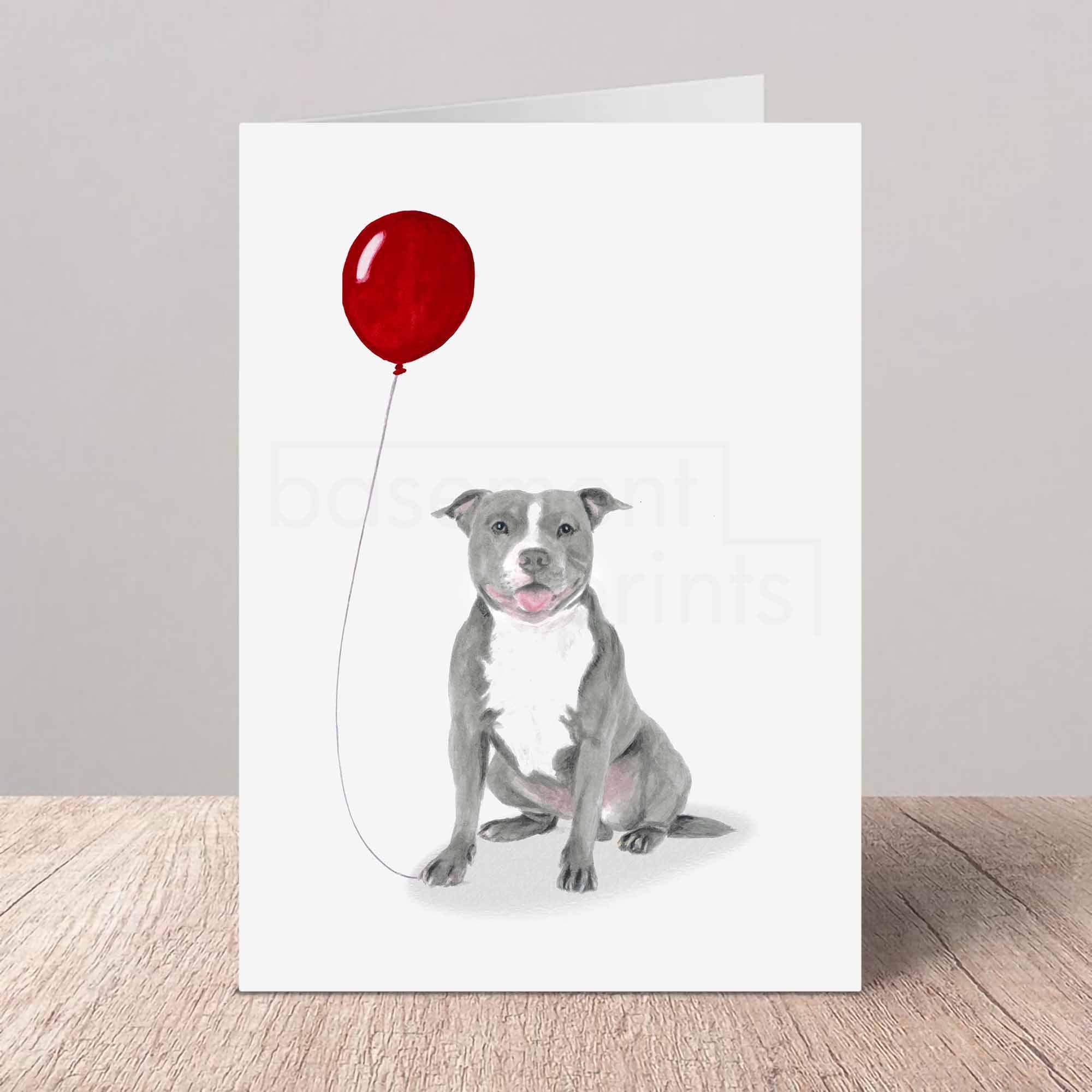 Greeting card with a grey Staffordshire Bull Terrier holding a red balloon on a white background