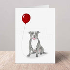 Greeting card with a grey Staffordshire Bull Terrier holding a red balloon on a white background