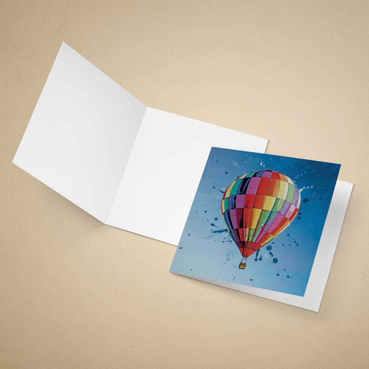 An open white greeting card on a beige background, showing a printed illustration of a colorful hot air balloon against a blue sky on the front.