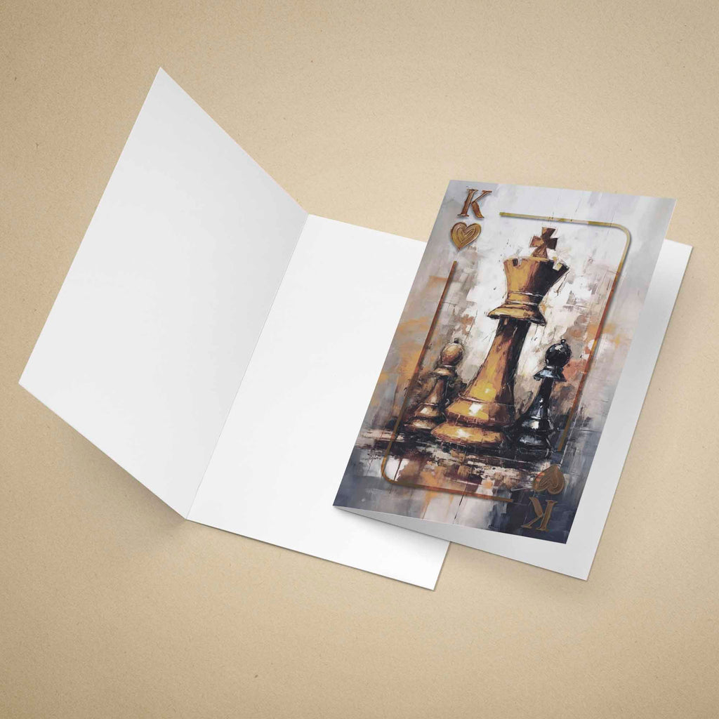 An open white greeting card lies on a beige background, showing a printed illustration of chess pieces on the front. The card design features a gold king and black pawns against a textured gray and gold background.